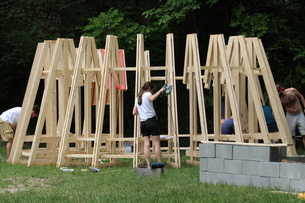 Workers and volunteers assembling the wooden modular frames of the structure in an outdoor setting, demonstrating the self-construction process 