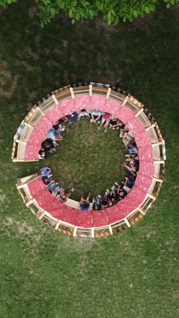 A direct overhead drone shot showing children and teachers sitting in a circle inside the completed modular classroom 