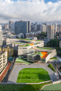 High-angle view of the school’s colorful, stepped roof landscape and its green athletic field, demonstrating a new typology for subtropical schools