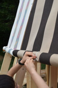 A child's hands tying a white cord to secure the striped fabric curtain to the wooden frame of the classroom