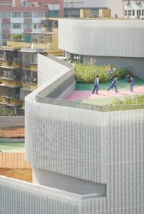 Detail of the school's curved, perforated metal facade overlooking students playing on a colorful outdoor terrace