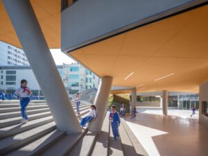 Students playing on wide concrete stairs beneath a massive cantilevered platform supported by angled columns