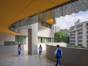 Students walking along a curved balcony featuring a bright yellow ceiling and decorative perforated sun screens
