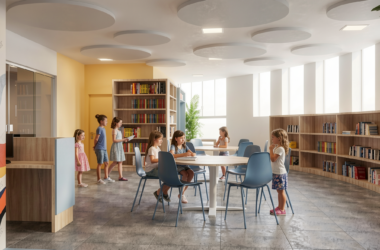 Children sitting at round tables in a bright school library, highlighting large windows for natural lighting and circular sound-absorbing ceiling panels designed to improve acoustic comfort