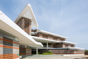Angular view of Rane Vidyalaya's modern exterior featuring white concrete overhangs and layered red and grey brickwork.
