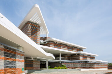 Angular view of Rane Vidyalaya's modern exterior featuring white concrete overhangs and layered red and grey brickwork.