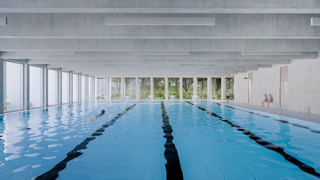 The school’s swimming pool area featuring multiple lanes, a concrete ceiling, and large windows that provide soft, diffused light