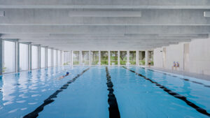 The school’s swimming pool area featuring multiple lanes, a concrete ceiling, and large windows that provide soft, diffused light