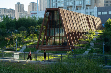 A side view of the tea house's rhythmic wooden facade, appearing as a natural extension of the surrounding park greenery