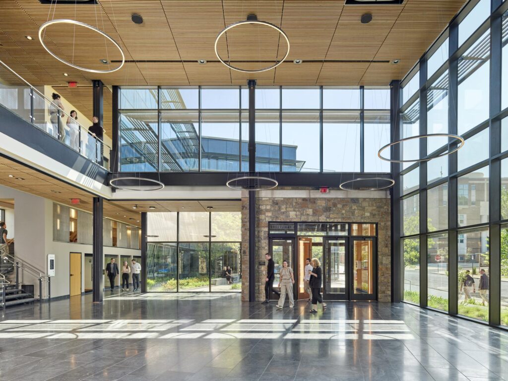 A wide view of the spacious, double-height entrance lobby featuring full-height glass walls, circular pendant lights, and a natural stone accent wall