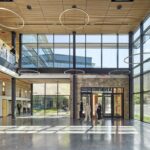 A wide view of the spacious, double-height entrance lobby featuring full-height glass walls, circular pendant lights, and a natural stone accent wall