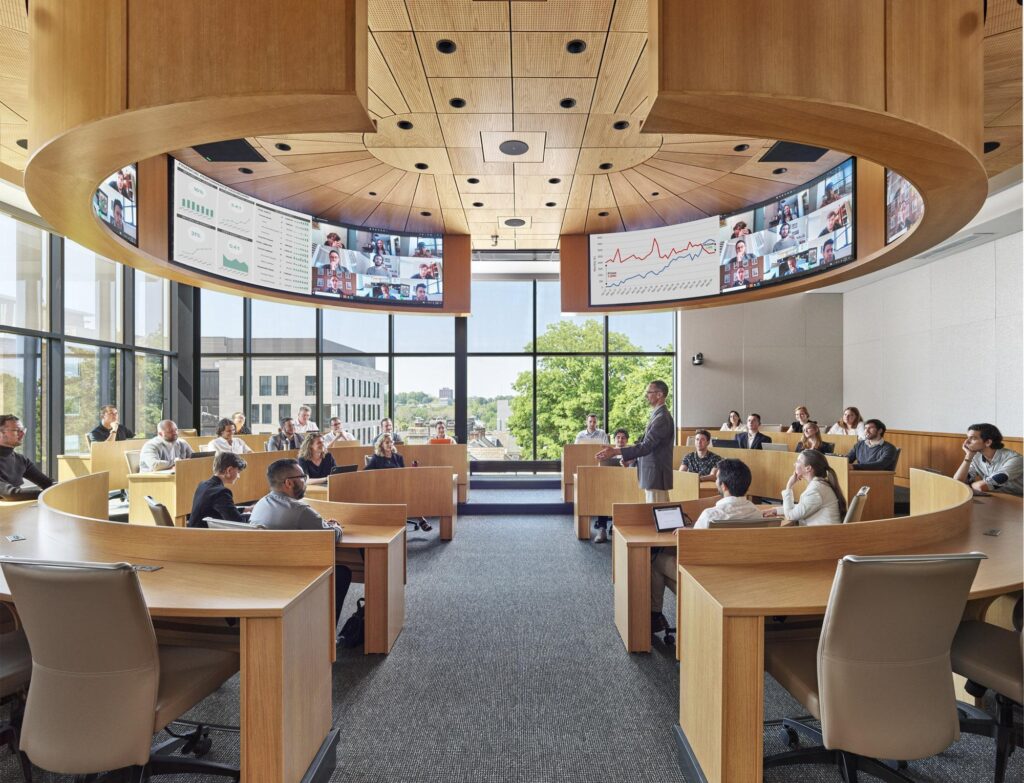 A circular, podium-less lecture hall mimicking a corporate setting, with four LED arrays hanging above for maximum screen visibility