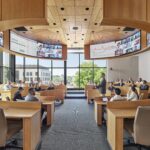 A circular, podium-less lecture hall mimicking a corporate setting, with four LED arrays hanging above for maximum screen visibility