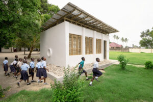 A white exterior wall of the library featuring a circular built-in reading nook with a red cushion, adjacent to a curved wall of translucent perforated panels that filter daylight
