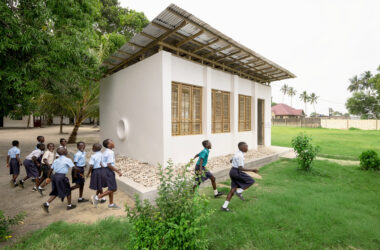 A white exterior wall of the library featuring a circular built-in reading nook with a red cushion, adjacent to a curved wall of translucent perforated panels that filter daylight