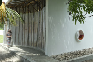 A white exterior wall of the library featuring a circular built-in reading nook with a red cushion, adjacent to a curved wall of translucent perforated panels that filter daylight