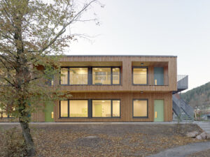 An exterior shot of the kindergarten’s sustainable timber facade, showing large windows and the integration of the building into the sloped site