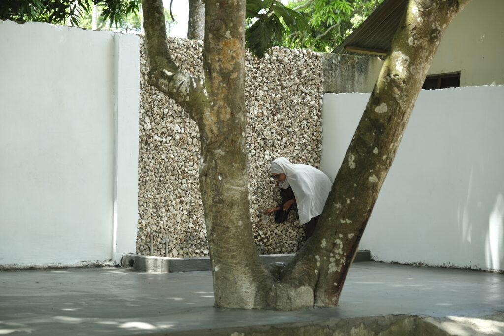 A person using the integrated water feature built into a textured coral stone wall in the courtyard, a design element symbolically associated with life and knowledge