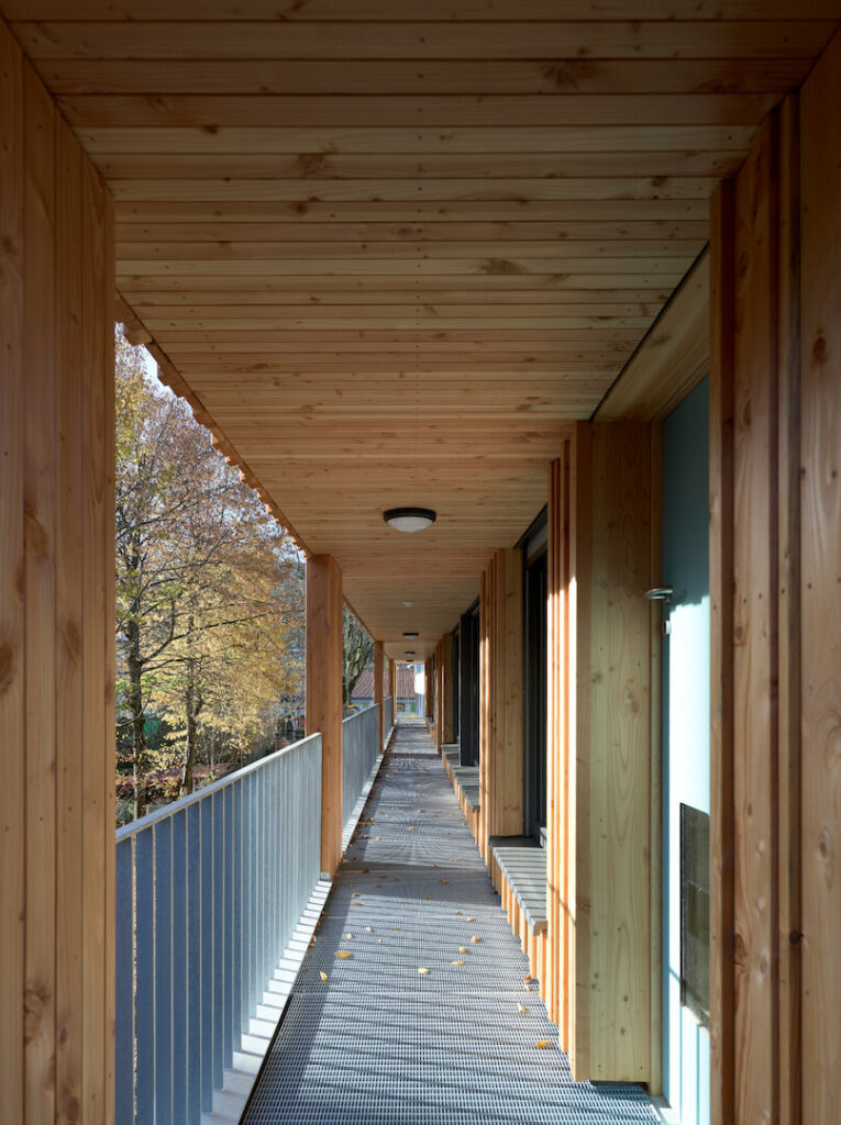 A view looking down the length of the external access gallery, showcasing the wooden structural pillars and metal floor grating