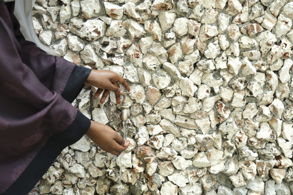 Close-up of hands using a metal tap mounted on a textured stone wall, part of the library’s environmental strategy and cultural depth