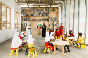 Interior of the library showing a non-hierarchical and flexible floor plan with low yellow and red stools, round wooden tables, and floor-to-ceiling bookshelves.