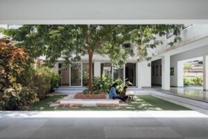 Students utilizing a shaded courtyard space for informal study, surrounded by lush green pockets and trees