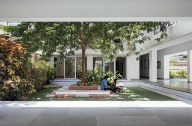 Students utilizing a shaded courtyard space for informal study, surrounded by lush green pockets and trees