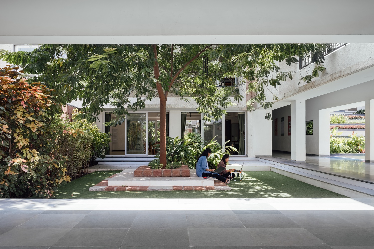 Students utilizing a shaded courtyard space for informal study, surrounded by lush green pockets and trees