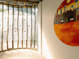 Interior shot highlighting the filtered daylight passing through perforated panels and a large, colorful circular mural depicting a cityscape on a white wall