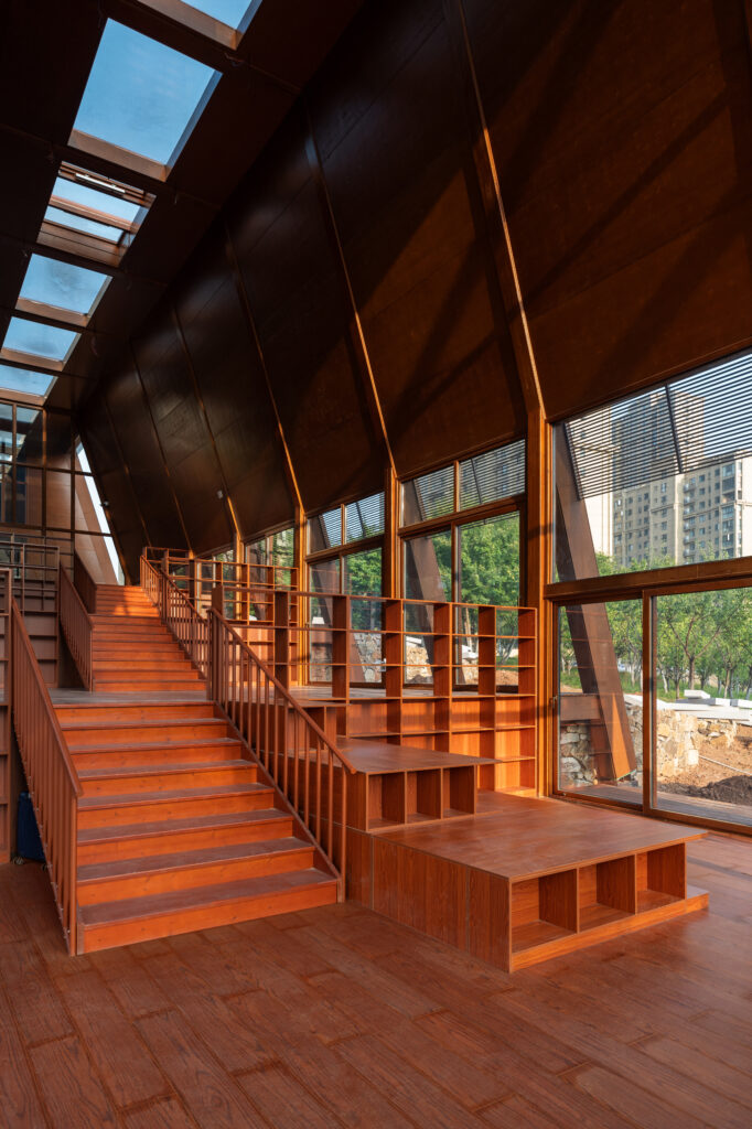 Looking down through the high-ceilinged interior of the tea house toward a large glass window that frames the park landscape and the library across the water