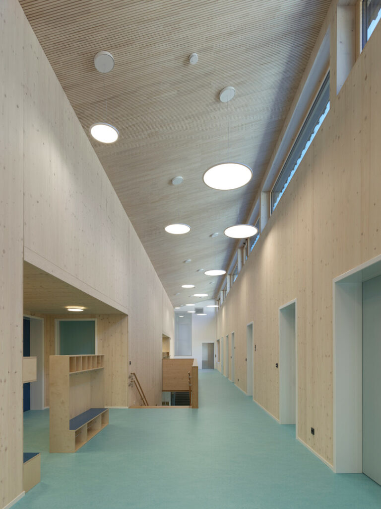 A bright interior corridor showcasing the high, sloping cross-laminated timber ceilings and natural wood walls