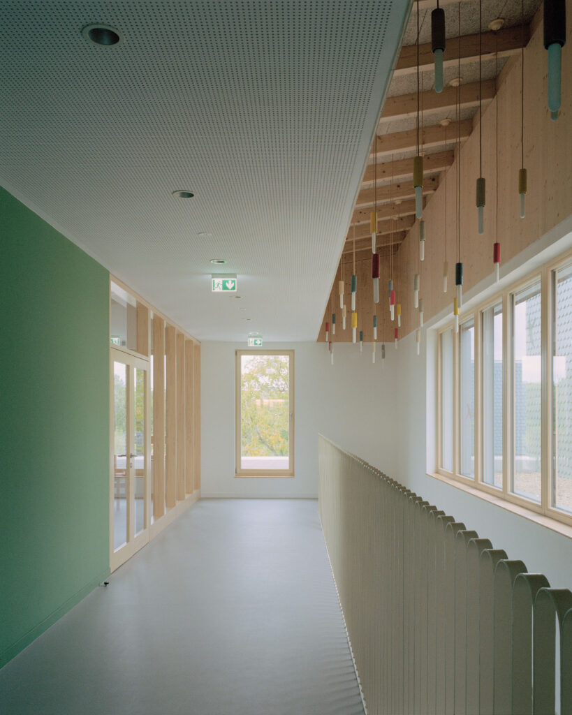 An interior hallway at Children’s Grove showing the predominance of natural wood, a vibrant green feature wall, and innovative lighting design for educational spaces