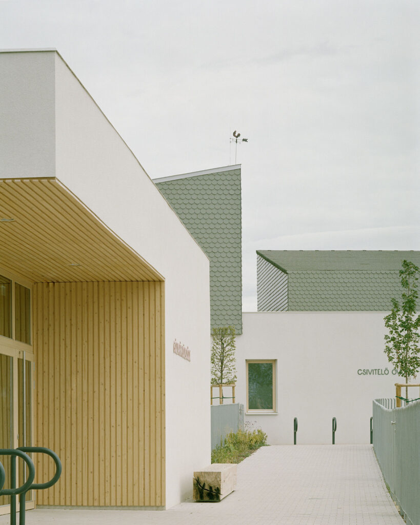 Close-up of the Children’s Grove entrance showing the interaction between natural wood cladding and textured green ceramic tiles on the facade
