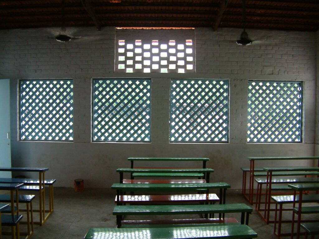  Interior of a classroom featuring green desks and continuous wooden jaali (lattice) windows for natural light and air penetration
