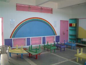 Interior of a vibrant nursery classroom featuring a rainbow wall mural and low colourful tables designed for holistic learning