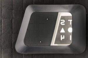 Looking up at a rectangular ceiling opening within a black textured surface, featuring alphabet-shaped cutouts that allow light to filter through for shadow play