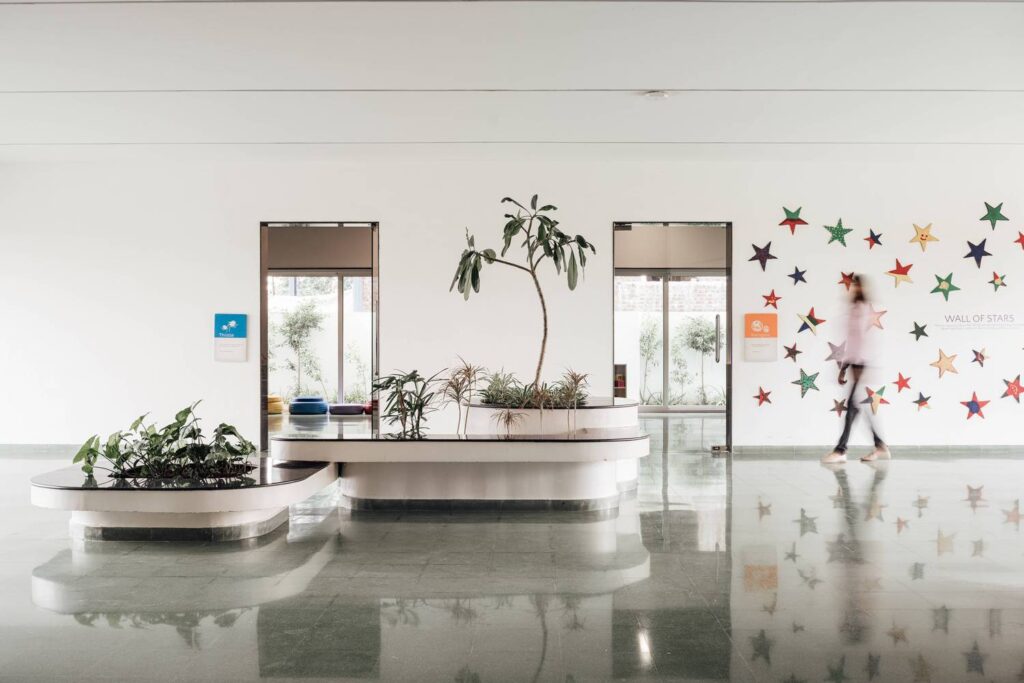 A bright indoor lobby featuring polished green stone flooring, a curved white planter with integrated seating, and a decorative wall display titled "Wall of Stars"