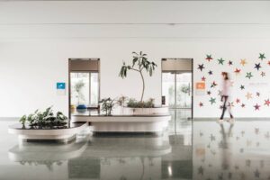 A bright indoor lobby featuring polished green stone flooring, a curved white planter with integrated seating, and a decorative wall display titled "Wall of Stars"