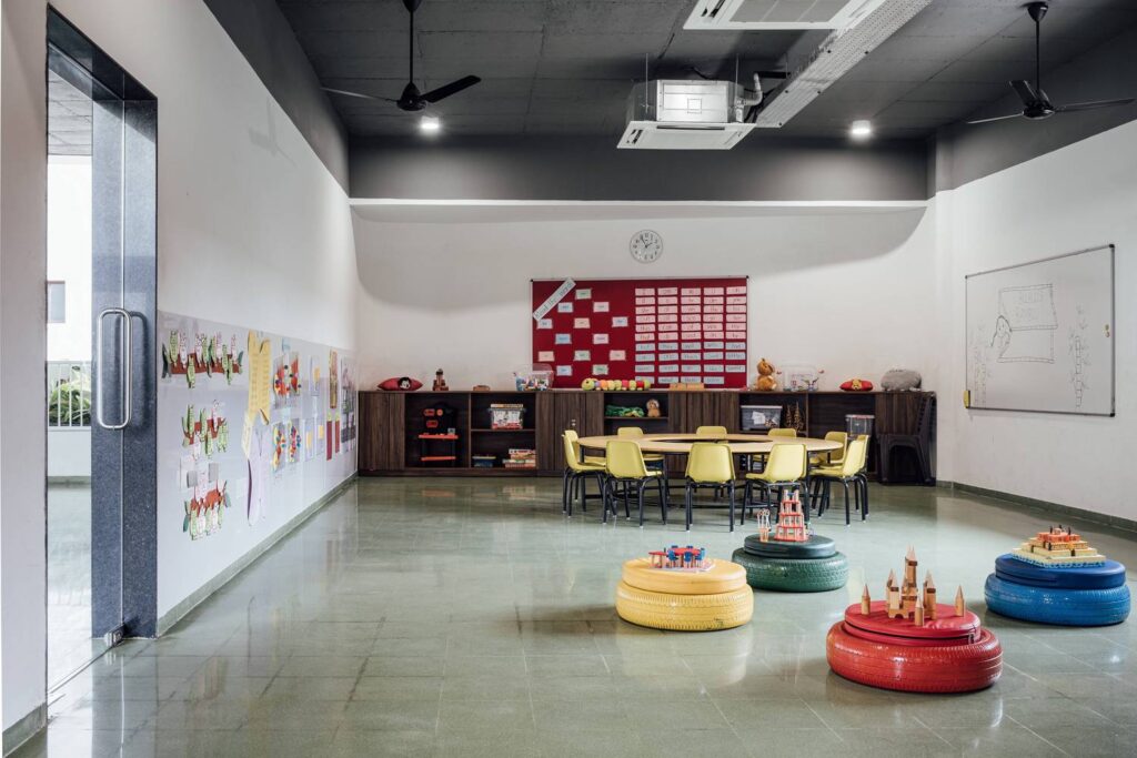 A kindergarten classroom featuring exposed ceiling ducts, seating made from upcycled colorful tires, and handmade cement tiles on the floor to stimulate sensory perception