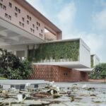 A ground-level shot of a blooming lotus pond in the foreground with the school’s stone and creeper-covered facade in the background