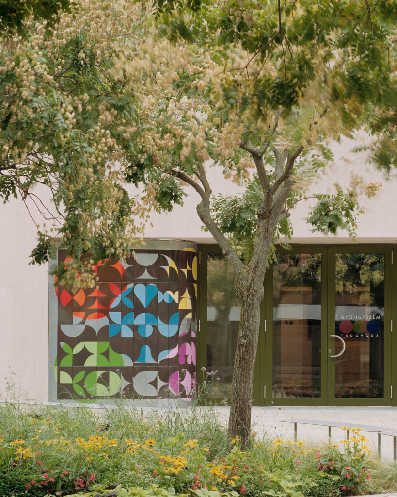 Close-up of a vibrant, geometric fire-enamel art piece integrated into the facade next to the main entrance glass doors
