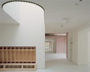 Bright white interior hallway showing wooden storage cubbies and a large circular opening in the ceiling leading to a naturally lit mezzanine level
