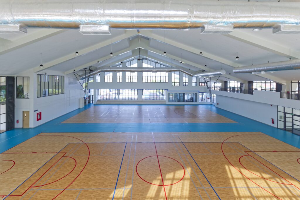 Wide interior view of the 5000m2 Gateway Project gymnasium in Laos, showcasing two full-sized basketball courts and tiered permanent seating for community events