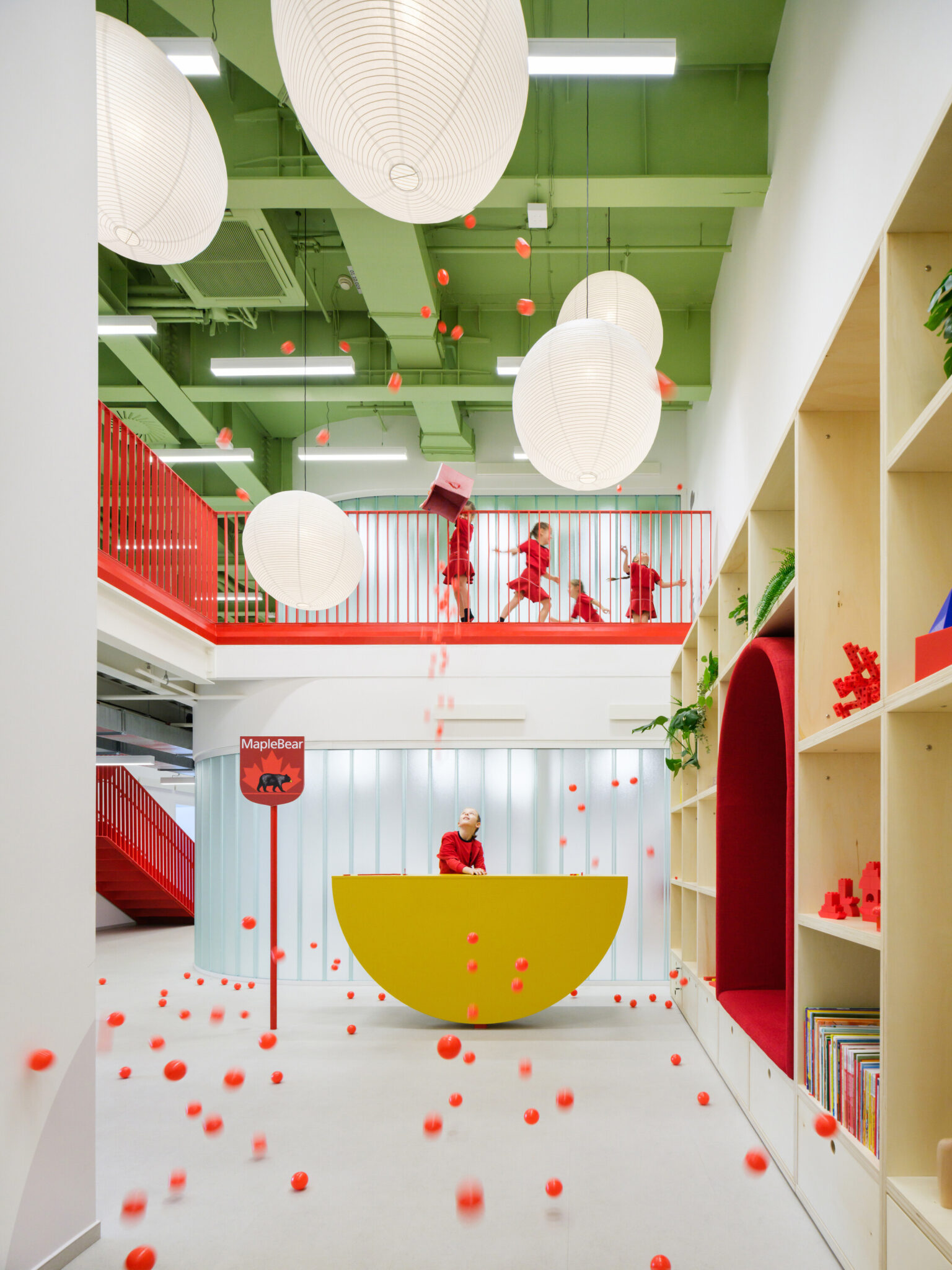 A wide view of the two-story entrance hall featuring exposed green steel beams, large white globe pendant lights, and a yellow semicircular reception desk.