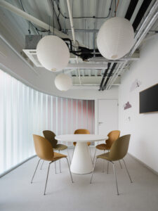 A bright meeting or reading corner with a round white table, earthy-toned chairs, and cloud graphics on the wall.