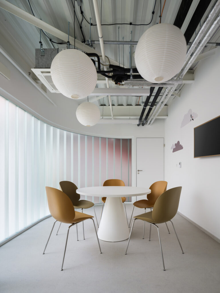 A bright meeting or reading corner with a round white table, earthy-toned chairs, and cloud graphics on the wall.