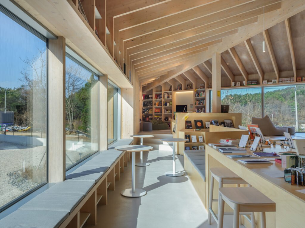 Built-in wooden bench seating along a large window with small round tables in a sunlit library.