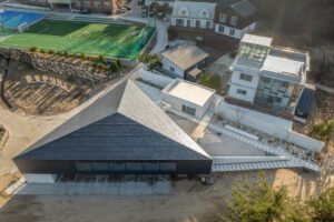 A bird's-eye view of a modern black triangular library building situated on a sloped site next to a sports field in South Korea.