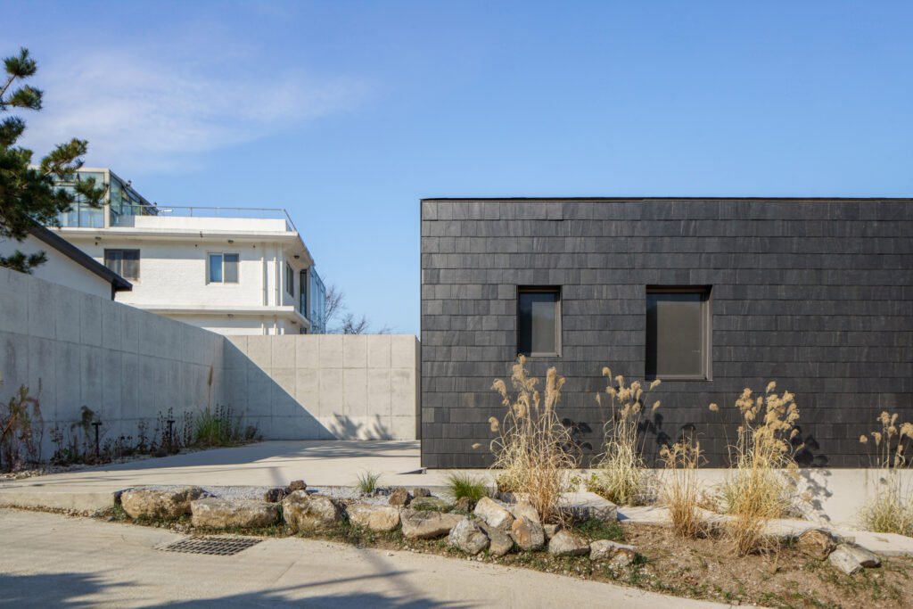 Exterior view of a building with dark slate-like stone cladding and a concrete wall under a clear blue sky.