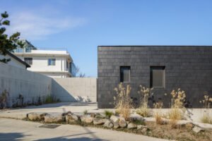 Exterior view of a building with dark slate-like stone cladding and a concrete wall under a clear blue sky.